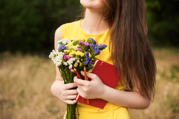 long-haired blond girl standing in the park and holding bouquet of flowers, a notebook and colored pencils in her hands