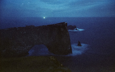 A dark view of the coastline from the lighthouse shining beam in the night in Iceland analog...