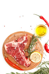 Raw t-bone steak on a wooden board with rosemary and spices on a white background. Top view.
