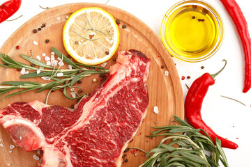 Raw t-bone steak on a wooden board with rosemary and spices on a white background. Top view.