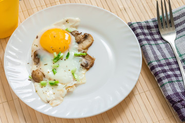 Fried egg with mushrooms champignons on a white plate sprinkled with green onions.