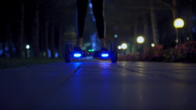 A girl riding a gyro scooter in the evening. Turned on lights in the evening park. Leisure