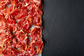 Appetizing slices Iberian ham in the foreground. Olive oil. Black background. Space to insert your...
