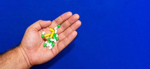 A lot of different pills in a male hand close-up. Blue blurred background. Pharmaceutical business concept. Healthcare industry. Sick person. Free space for text.