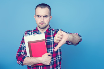 Angry school teacher with books, showed a thumb down, portrait, blue background, copy space