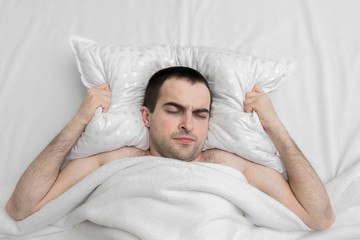 Young man sleeping in the bedroom, guy's having a nightmare, white blanket, top view, copy space