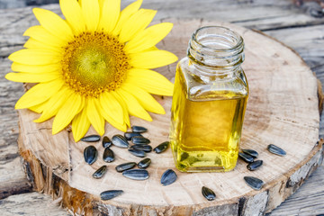 Organic sunflower oil in a glass jar with seeds and fresh flowers on a wooden background. Healthy foods and fats.