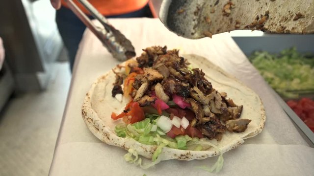chef preparing shawarma. Putting grilled meat cuts over the lettuce sauce and tomatoes