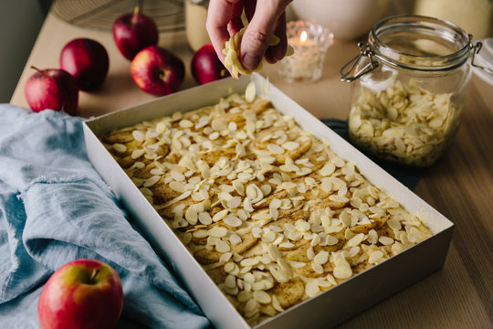 Woman scattering almond flakes on apple cake