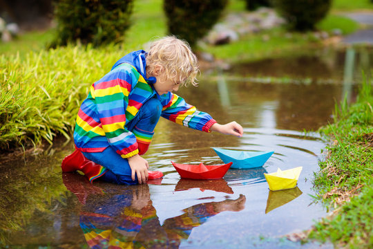 Child with paper boat in puddle. Kids by rain.