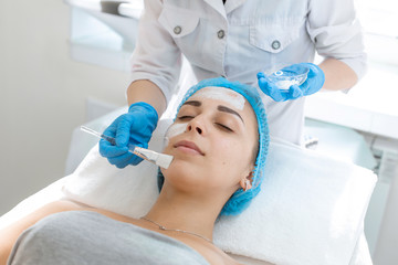 A professional cosmetologist applies a nourishing cream on the patient's face. Moisturizing, cleaning and facial skin care. Cosmetic procedures
