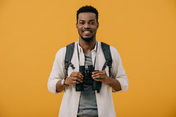 cheerful african american man holding binoculars isolated on orange