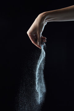 The hand of the girl pours silver powder on a black background with copy space. Creative photo as a layout.