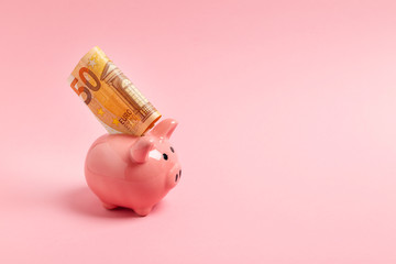 Pink piggy bank with fifty euros on a pink background.