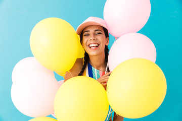 Image of happy smiling woman wearing cap looking at camera while holding air balloons