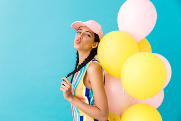 Image of happy seductive woman wearing cap making kiss lips while holding air balloons