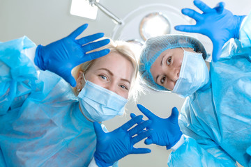 Crazy scary and funny doctors surgeons dentists in masks with gloves and coats scare and tease on camera. A nightmare patient. Portraits of doctors close-up. First-person view. Lamp background