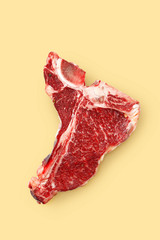 Raw t-bone steak on a yellow background.