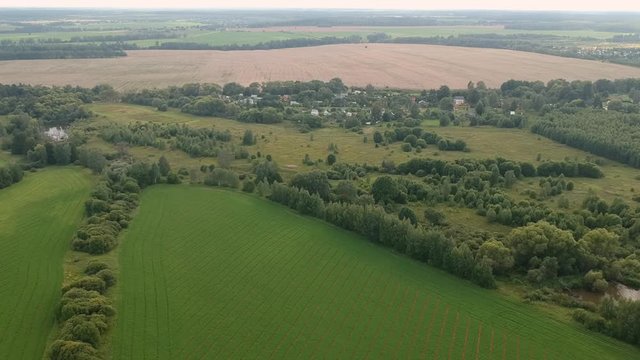 Aerial View of the green fields, rooftops of a little village and roads.