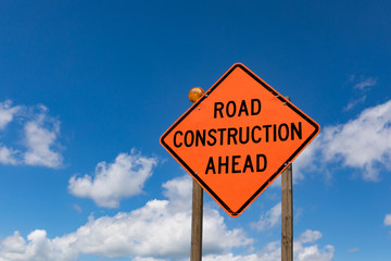 closeup of road construction ahead sign and warning light with blue sky and clouds in background