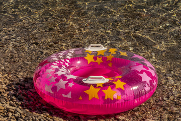 Summer beach composition. Pink  inflatable float with stars on pebble, shingle, boulder sea ...