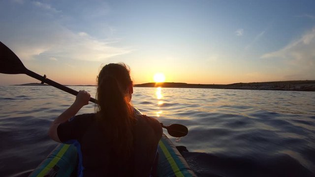 Woman paddling her sea kayak towards the setting sun