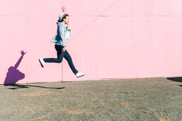 Young man in front of pink construction barrier, jumping in the air
