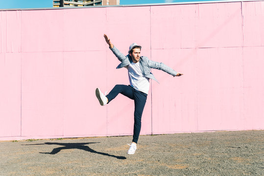 Young man in front of pink construction barrier, jumping in the air