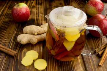 Hot tea with apples, cinnamon  and ginger in the glass teapot  on the brown  wooden background. Healthy drink.