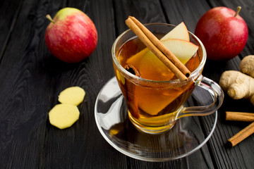 Hot tea with apples, cinnamon  and ginger in the glass cup on the black  wooden background. Healthy...