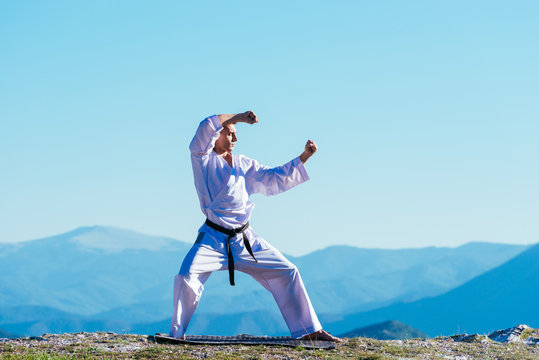 Blond karate athlete does kata on top of a mountain while performing a line up of kicks, punches and blocks on top of a mountain on a sunny day.