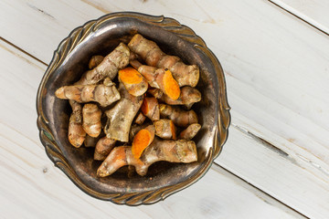 Lot of whole lot of slices of bright turmeric rhizome in old iron bowl flatlay on white wood