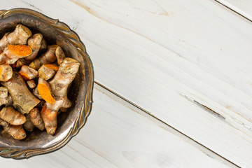 Lot of whole lot of slices of bright turmeric rhizome copyspace on right in old iron bowl flatlay on white wood