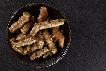 Lot of whole bright turmeric rhizome on grey ceramic plate flatlay on grey stone