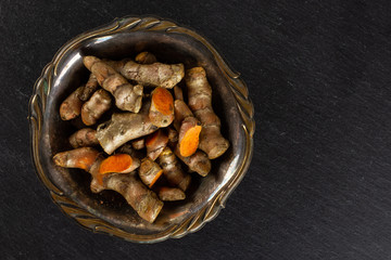 Lot of whole lot of slices of bright turmeric rhizome in old iron bowl flatlay on grey stone