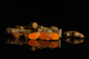 Group of lot of whole three slices of bright turmeric rhizome isolated on black glass