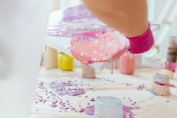 Woman painter holding hair dryer while female beginnres studying creating fluid acrylic abstract painting in art therapy class, dropping paints on canvas. Teamwork, study, art therapy concept.