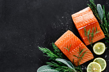 Salmon. Fresh raw salmon fish fillet with cooking ingredients, herbs and lemon on black background, top view - obrazy, fototapety, plakaty
