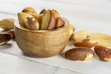 Lot of whole unshelled brazil nut near and in wooden bowl on white wood