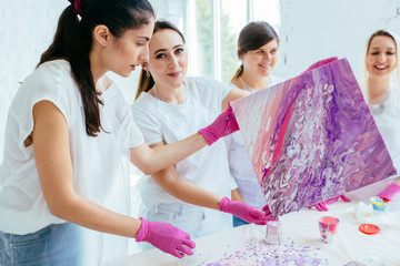 Group of five female creating and slowly whirling canvas with liquid acrylics abstract painting in...