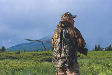 Hunter with a hat and a gun in search of prey in the steppe against the backdrop of a mountains