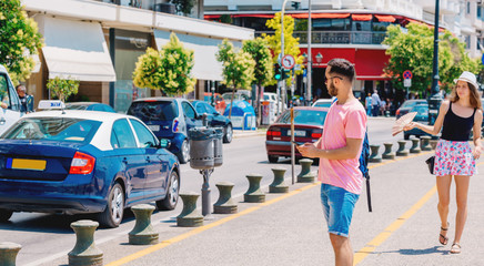 Student calling a taxi while wearing a backpack on his shoulder and standing on a city boardwalk.