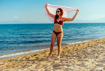 Fototapeta na wymiar Portrait of attractive girl playing with pink scarf on windy beach