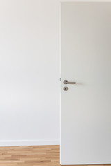 Open white door with a gray chrome handle and keyhole against a white wall in the room