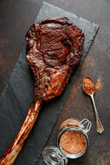 Top view of grilled beef steak Tomahawk with spices on a black slate. Flat lay, dinner concept.