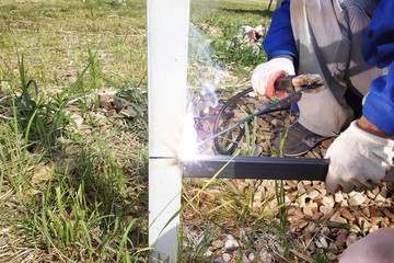 Worker with welding machine welds the fence around the house.
