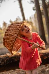 The little girl in a wood with a basket costs on beautiful many leaves of a maple