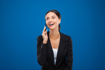 Portrait of a beautiful businesswoman laughing while speaking on phone, isolated on blue background.