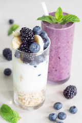 Smoothies of banana, blueberry, blackberry, oatmeal and yogurt and ingredients in two glasses on a light background