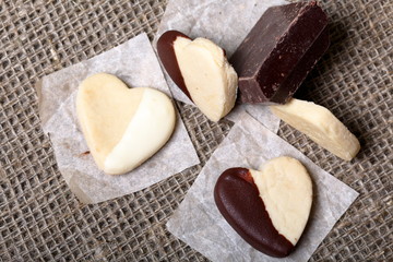 Heart shaped biscuit cookies. Some cookies are decorated with dark chocolate. Some cookies are decorated with white chocolate. Nearby a piece of dark chocolate. Lie on a coarse linen cloth.